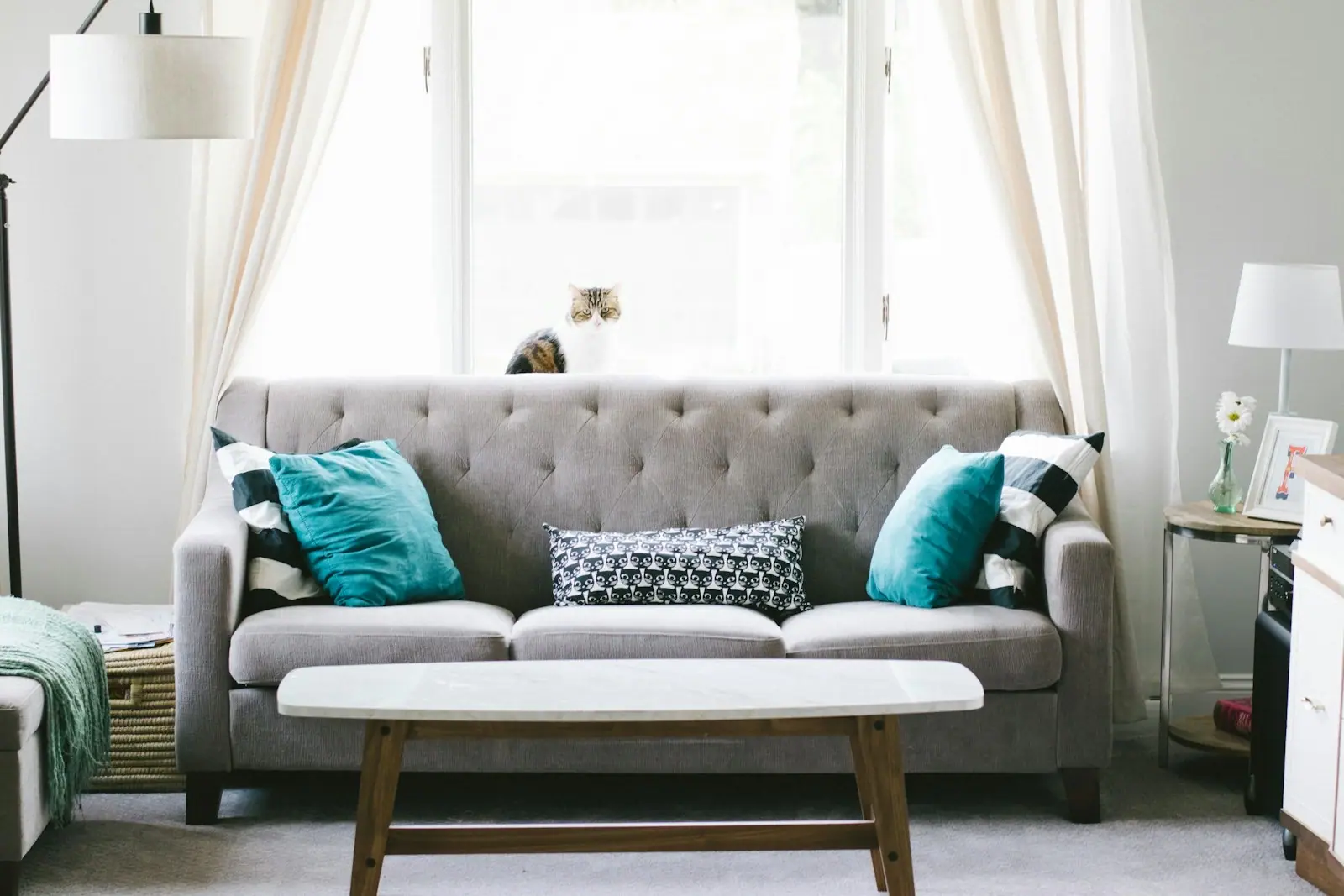 Grey button-tufted three-seater fabric sofa with teal and patterned cushions